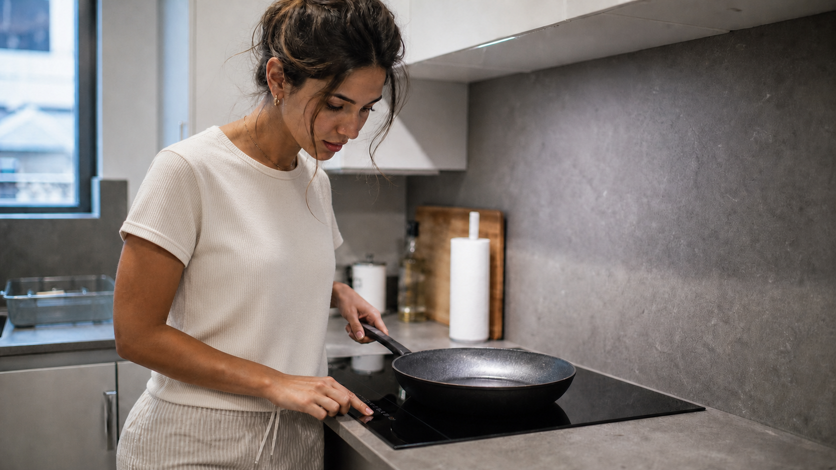A guest studies the controls of an induction hob while holding a pan in a compact short-let kitchen.