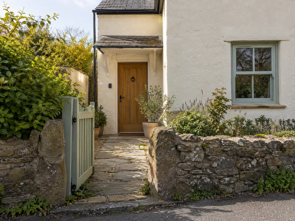 Open green pedestrian gate on the left of a cream-coloured house, with a path to the front door and a key safe beside it.